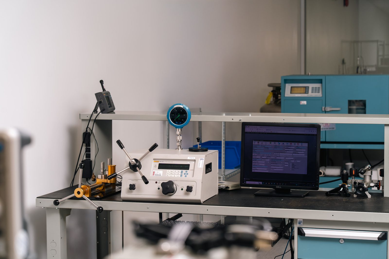 Calibration bench with pressure calibrator, blue digital gauge, and monitoring software